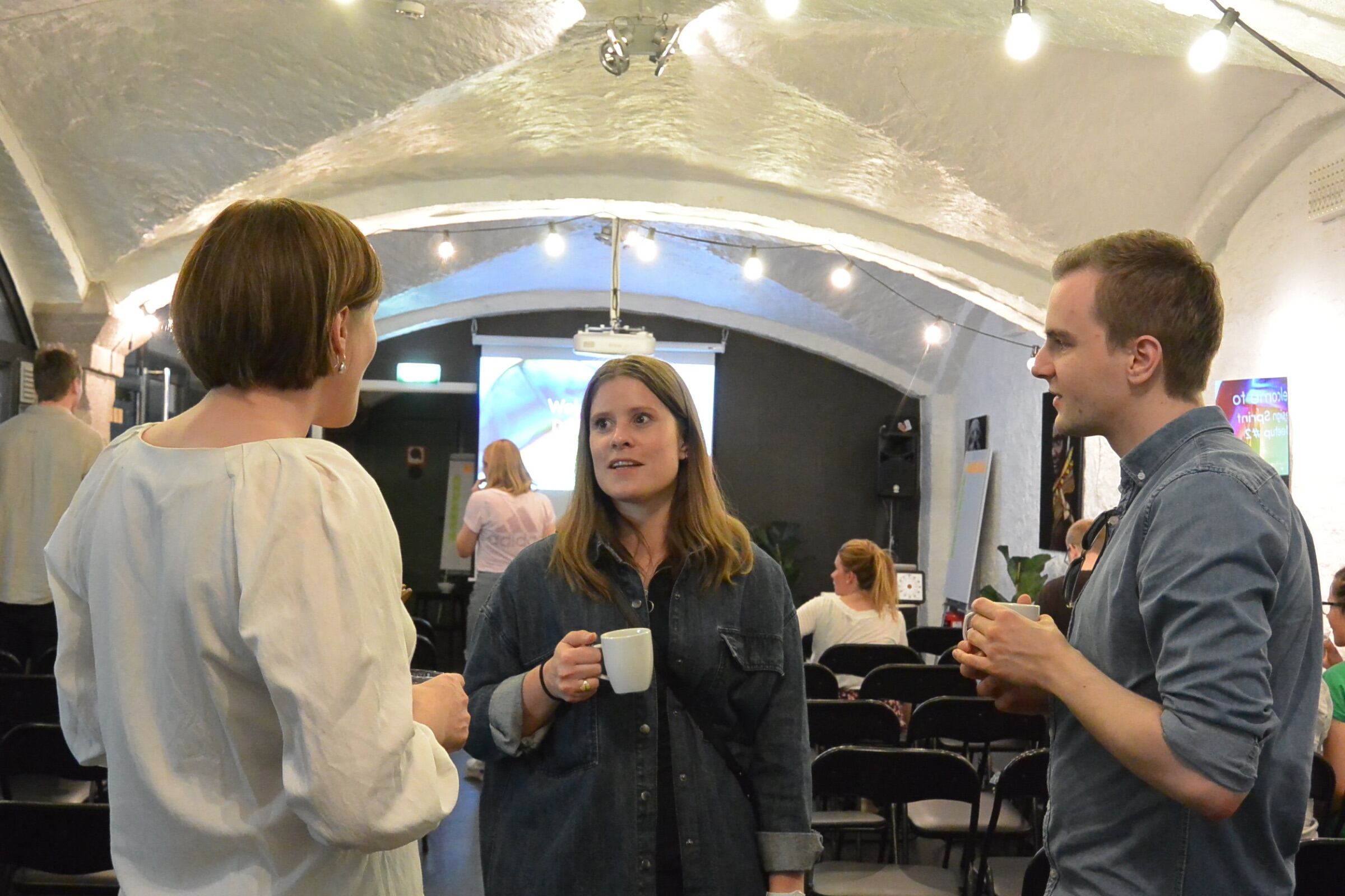 Kollegaer i samtale med kaffekopper, en presentasjon i bakgrunnen